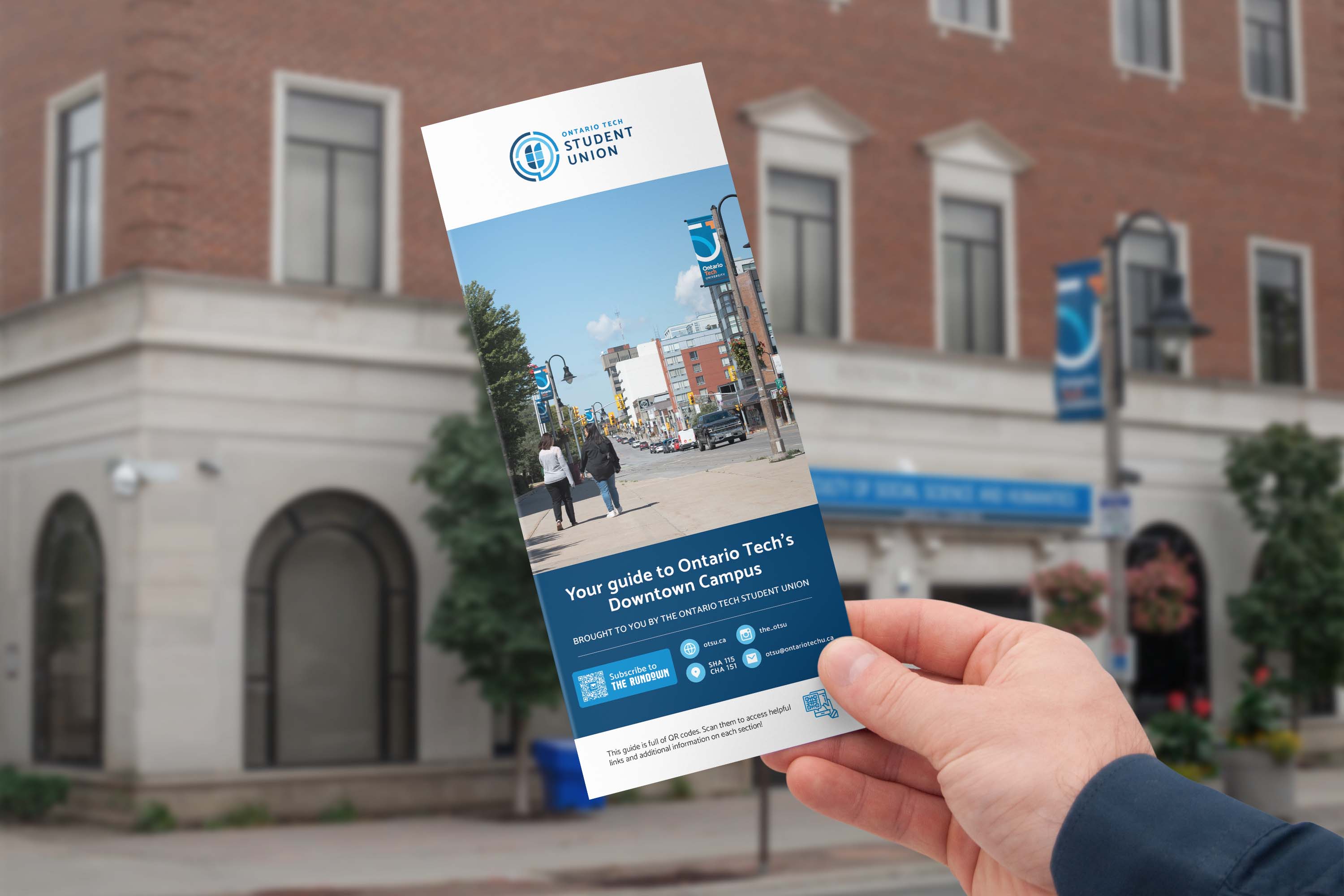 The OTSU downtown resource guide held in front of an Ontario Tech University building in downtown Oshawa.